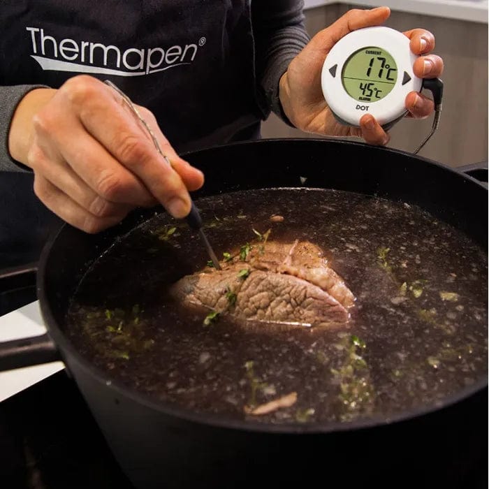 Une femme fait cuire de la viande dans une marmite avec un Thermomètre de four numérique DOT de Thermometre.fr.